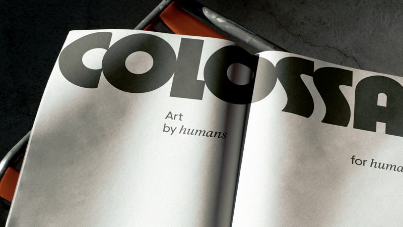 Colossal, art by humans for humans, printed on newsprint resting on a bench